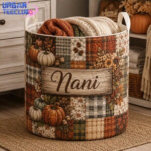 May include: A cylindrical fabric storage basket featuring a patchwork design of pumpkins, autumn leaves, and plaid patterns in orange, brown, and cream tones. A central wooden-look label displays the name Nani in a dark brown cursive script.