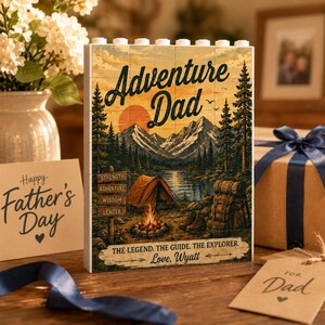 May include: A rectangular block display featuring a printed outdoor scene with mountains, a lake, a tent, and a campfire. The text reads Adventure Dad, Strength, Adventure, Wisdom, Leader, and The legend. The guide. The explorer. Love, Wyatt.