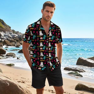 May include: Black button-down shirt and black shorts. The shirt features a repeating pattern of white cats wearing crowns, teal dinosaurs, and the word "DESPERADO" in red and white. The background is black.