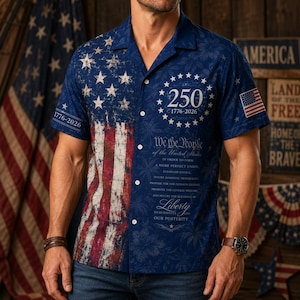 May include: A short-sleeve button-down shirt featuring a distressed American flag design on the left side and a dark blue background on the right. It displays the text 250 1776-2026, We the People, and a small American flag patch on the sleeve.