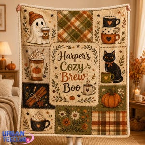 May include: A rectangular throw blanket featuring a patchwork design with illustrations of a ghost in a beanie, stacked mugs, a pumpkin spice latte, a black cat, cinnamon sticks, and pumpkins. The center text reads Harper's Cozy Brew Boo.