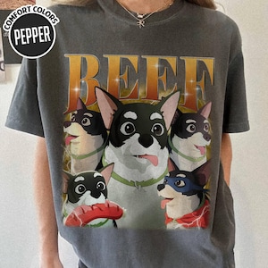 May include: Dark gray t-shirt featuring a cartoon graphic of several dogs with the word "BEEF" in large, gold letters. The dogs have black and white fur, with some wearing accessories. The shirt has a crew neck and short sleeves.