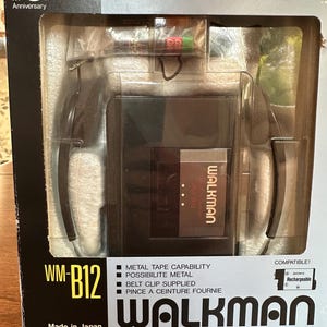 May include: A black Sony Walkman WM-B12 cassette player in its original packaging. The box features the 10th Anniversary logo, the model number, and text indicating metal tape capability and a belt clip. The device is visible through a clear window.