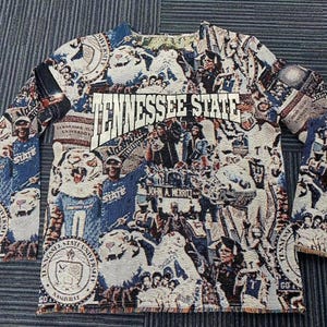 May include: A blue and white tapestry featuring the Tennessee State University logo and various images, including a tiger, a football player, and a graduation cap. The tapestry is made of woven fabric and has a fringed edge.