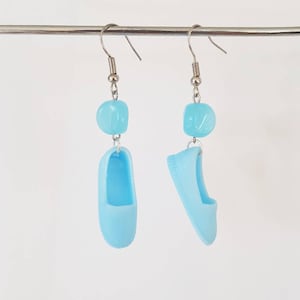 May include: A pair of light blue dangle earrings featuring a small shoe charm and a light blue bead.