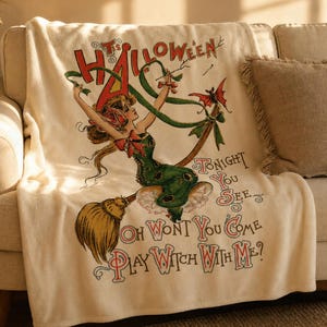 May include: A cream-colored throw blanket featuring a vintage-style illustration of a figure riding a broomstick. The text reads: It's Halloween Tonight You See, Oh Wont You Come Play Witch With Me? The design includes red, green, and brown accents.