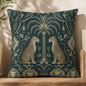 May include: Square cushion with a dark teal background featuring a symmetrical design. Two leopards face each other beneath a palm tree. The cushion has a detailed pattern with lions, peacocks, and floral elements.
