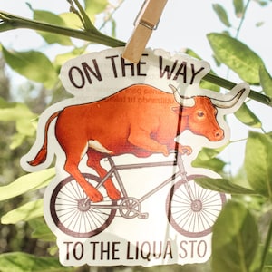 Pegatina divertida de un toro en bicicleta: «De camino a la estación Liqua». Vinilo del oeste.
