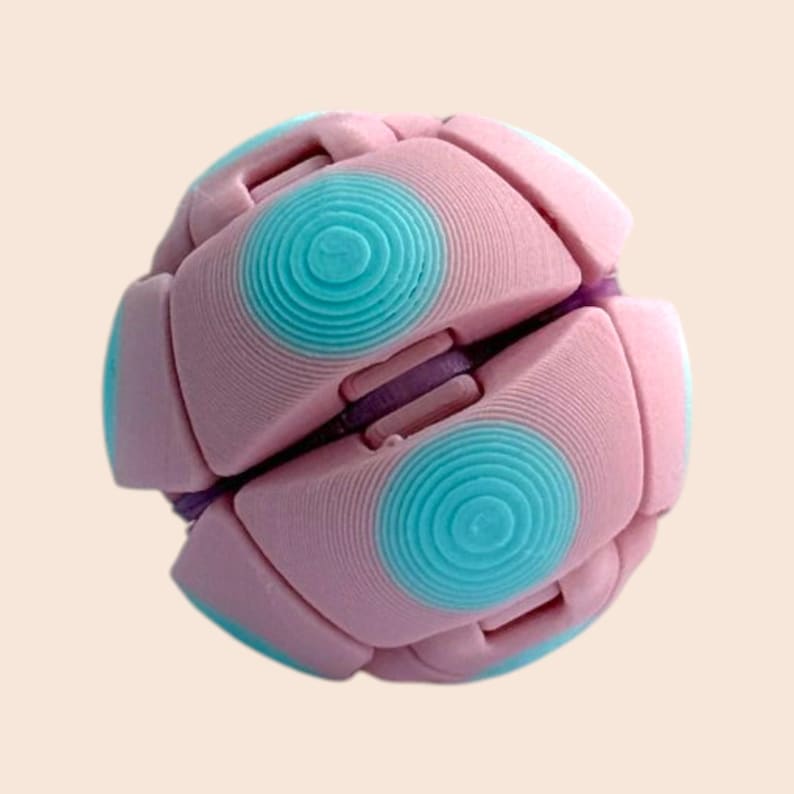 Pu&ograve; includere: Un giocattolo a forma di palla rosa e turchese con un design unico. Il giocattolo presenta una serie di pannelli ad incastro, ciascuno con un design circolare turchese. La palla &egrave; di colore rosa chiaro con accenti turchesi e viola. Il giocattolo &egrave; progettato per essere manipolato e giocato.