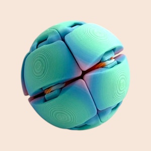 Pu&ograve; includere: Un giocattolo puzzle sferico multicolore. Il giocattolo &egrave; composto da diversi pezzi quadrati arrotondati in tonalit&agrave; di verde acqua, blu e rosa. Ogni pezzo presenta un motivo a cerchi concentrici. Il giocattolo &egrave; progettato per essere manipolato.