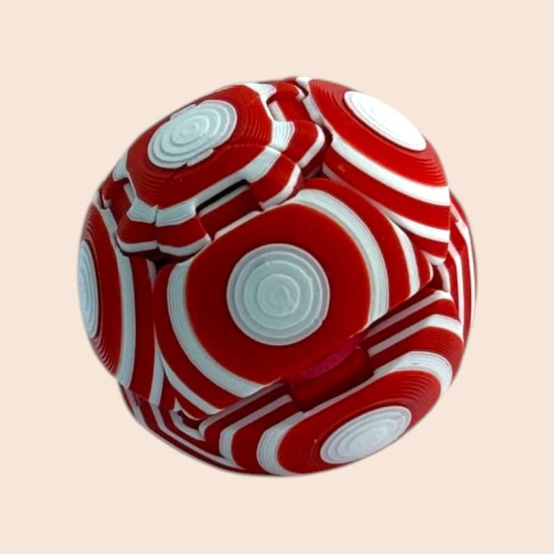 Pu&ograve; includere: Un giocattolo puzzle sferico rosso e bianco con un motivo a strisce. Il design del giocattolo presenta cerchi concentrici e linee curve, creando un aspetto visivamente accattivante e complesso. La combinazione di colori &egrave; un'audace combinazione di rosso e bianco.