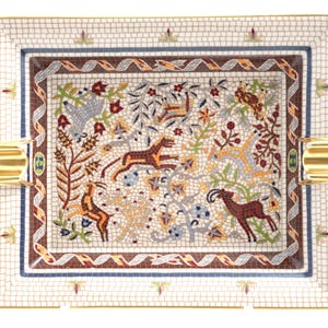 May include: A rectangular porcelain ashtray featuring a detailed mosaic-style pattern of various animals, including deer and a large cat, surrounded by floral motifs. The border has a white grid design with gold accents and two gold-toned rests.