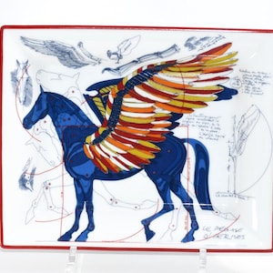 May include: Rectangular white ceramic tray with a red border. The tray features a blue Pegasus with colorful wings, and sketches of the horse. The text "LE PEGASE D'HERMES" is at the bottom right.