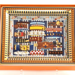 May include: A rectangular decorative tray with a colorful design. The tray features a blue background with various belt designs in brown, yellow, and blue. The tray is framed with orange, gold, and blue borders. The tray is presented in an orange box.