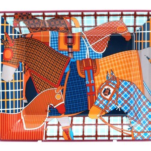 May include: A rectangular porcelain tray featuring a vibrant graphic print of multiple horses wearing checkered and plaid blankets in shades of orange, blue, and dark brown, set against a grid-patterned background with a deep maroon border.