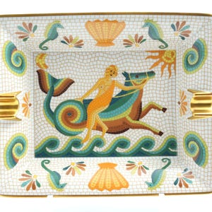 May include: A rectangular porcelain tray featuring a mosaic-style design of a figure riding a sea creature over waves. The border includes seahorses, shells, and gold-toned accents on the sides. The central illustration depicts a sun and moon.