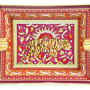 May include: Rectangular decorative ashtray with a vibrant design. The center features a yellow and black tiger against a magenta background with floral and sun motifs. The border is red with gold accents.