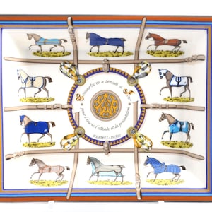 May include: A square, decorative scarf with a white background featuring illustrations of horses in various colors and blankets. The scarf has a brown and blue border, with text and equestrian-themed details.