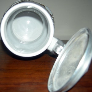 May include: A white ceramic beer stein with a metal lid. The stein has a traditional design with a raised handle and a round body. The lid is hinged and has a small knob on top.