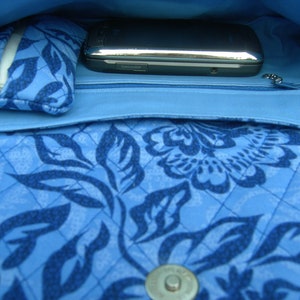 K&ouml;nnte beinhalten: Eine blaue gesteppte Handtasche mit Blumenmuster. Die Tasche hat eine Rei&szlig;verschlusstasche und ein Handyfach.