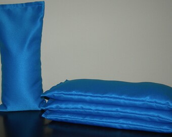 Könnte beinhalten: Vier blaue Satin-Kissenbezüge, die übereinander gestapelt sind. Ein einzelner blauer Satin-Kissenbezug steht links neben dem Stapel.
