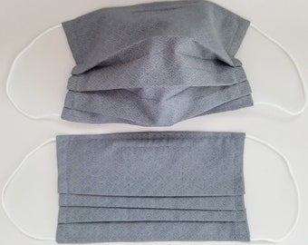 May include: Two gray face masks with white elastic ear loops. The masks have a geometric pattern and are pleated.