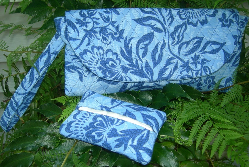 K&ouml;nnte beinhalten: Eine blaue gesteppte Clutch mit Blumenmuster und einer passenden kleineren Tasche. Die Clutch hat einen langen Riemen.