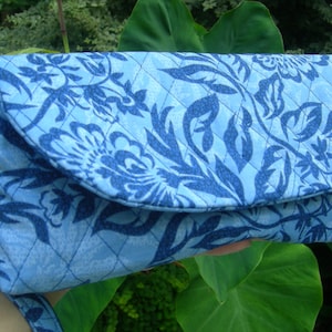 K&ouml;nnte beinhalten: Eine blaue gesteppte Clutch mit Blumenmuster. Die Clutch hat einen Klappverschluss und einen Riemen.