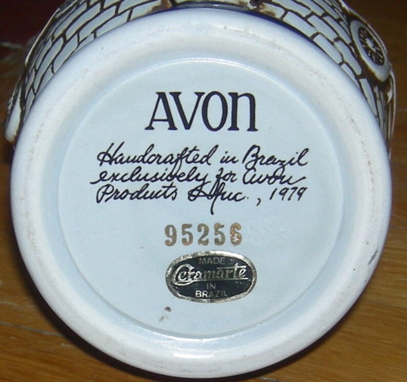 May include: White ceramic Avon bottle with a blue and white design. The bottom of the bottle has the text "AVON", "Handcrafted in Brazil exclusively for Avon Products Afric, 1979", "95256", and "Made in Brazil" with the Cramarle logo.