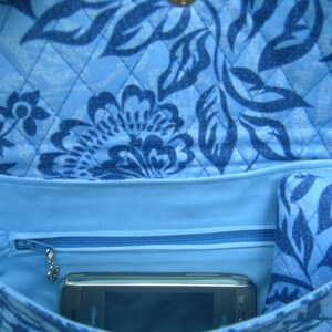 K&ouml;nnte beinhalten: Eine blaue gesteppte Tasche mit einem Blumenmuster. Die Tasche hat eine Rei&szlig;verschlusstasche und ein kleines Telefon im Inneren.