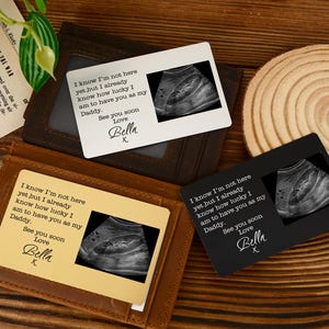 Puede incluir: Tres tarjetas de cartera con imágenes de ecografías y texto: "Sé que aún no estoy aquí, pero ya sé lo afortunado/a que soy de tenerte como mi papá. Nos vemos pronto Love Bella X." Las tarjetas son marrones, negras y blancas.