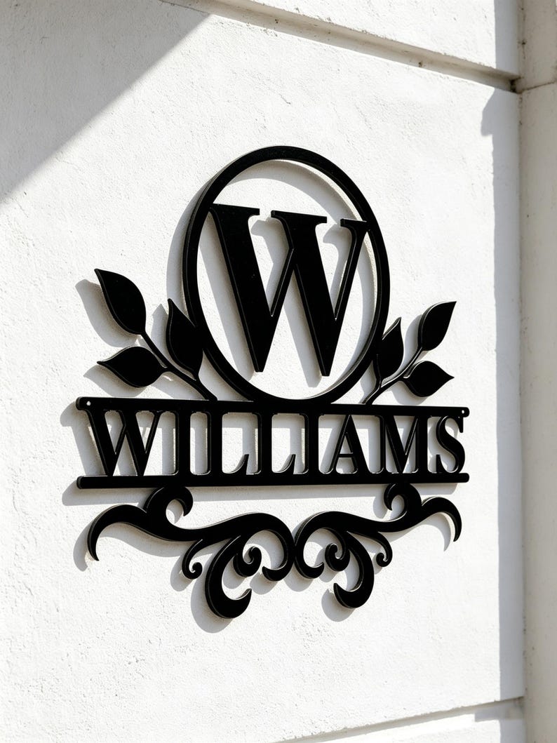 Pode incluir: Uma placa de parede em metal preto com uma letra W grande dentro de um c&iacute;rculo, com o nome WILLIAMS exibido numa barra horizontal abaixo. O design inclui detalhes de folhas decorativas em ambos os lados e volutas ornamentais na base.