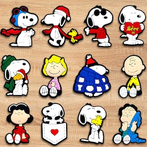 May include: A collection of colorful cartoon character figures, including Snoopy and friends. The figures feature various outfits and accessories, such as hats, scarves, and a heart-shaped item with the word "Love" on it. The figures are set against a wooden background.