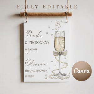 May include: A white sign with the text "Pearls & Prosecco" and "Welcome to Olivia's Bridal Shower" with a champagne glass illustration. The sign is hanging from a wooden dowel with twine.