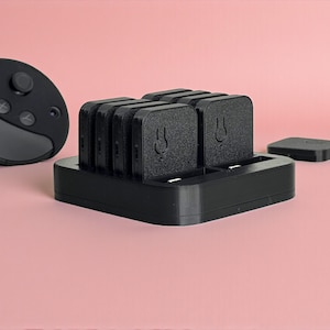 以下が含まれることがあります： 黒いVRヘッドセットコントローラーと充電ステーション。充電ステーションは黒色で、シンボルが付いた長方形のバッテリーパックを複数収納。小さな正方形のバッテリーパックも存在します。