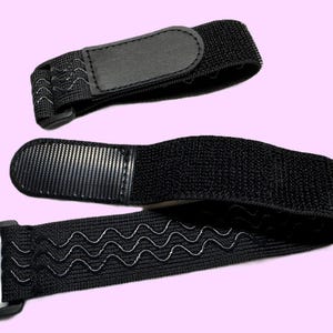 May include: Two black adjustable straps with silver zigzag stitching and a rectangular buckle. One strap has a small black leather patch, and the other has a larger patch. The straps are likely for securing items.