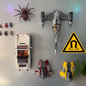 May include: A collection of Lego models and minifigures, including a white car, spaceships, and a large brown spider. A yellow warning sign with a magnet symbol is also present.