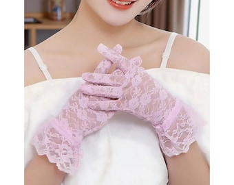 May include: Pale pink lace gloves with a floral pattern. The gloves have a ruffled edge at the wrist. The delicate design is visible on the fingers and the back of the hand. The gloves are a light, soft pink color.