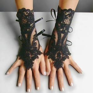 May include: A pair of black lace gloves featuring detailed floral designs and slender ribbon ties. These gloves, covering the wrist and part of the hand, present an elegant and stylish accessory.