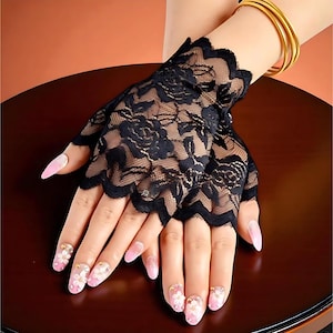 以下が含まれることがあります： 黒いレースのフィンガーレスグローブ。花柄とスカラップエッジが特徴です。ゴールドのブレスレットと合わせています。爪はピンクと白の花柄でペイントされています。