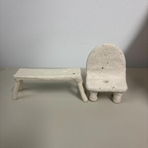 May include: A miniature off-white bench and a matching chair with a textured, speckled surface. Both pieces feature a rough, hand-formed appearance with four sturdy legs each, showcasing a consistent light beige color and a porous, matte finish.