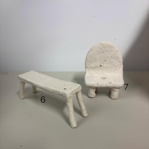 May include: A miniature off-white speckled ceramic bench labeled with the number 6 and a miniature off-white speckled ceramic chair labeled with the number 7. Both items feature a rough, textured surface and four sturdy legs.