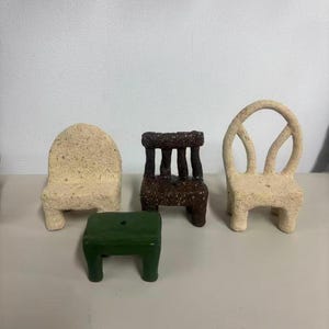 May include: A collection of four miniature furniture pieces including a beige textured chair with a solid back, a dark brown textured chair with a slatted back, a beige textured chair with an oval back, and a small smooth green rectangular stool.