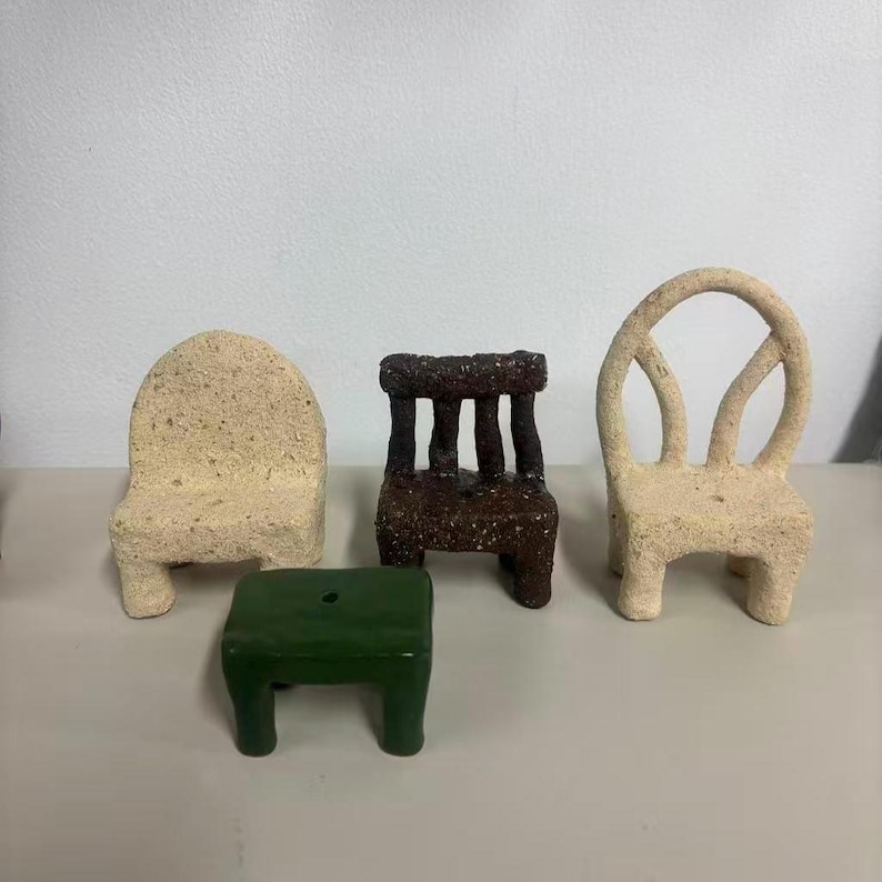 May include: A collection of four miniature furniture pieces including a beige textured chair with a solid back, a dark brown textured chair with a slatted back, a beige textured chair with an oval back, and a small smooth green rectangular stool.
