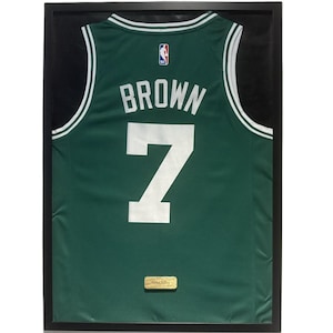 Puede incluir: Camiseta de baloncesto verde enmarcada con el nombre "BROWN" y el número "7" en blanco. La camiseta tiene ribetes blancos y verdes y un logotipo de la NBA. La camiseta se muestra en un marco negro.