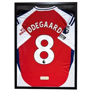 May include: Framed red and white soccer jersey with the name "ØDEGAARD" and the number "8" on the back. The jersey is displayed in a black frame. The jersey also has the text "VIS RWA" on the sleeve.