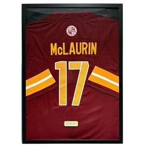 Pode incluir: Camisola de futebol bordô emoldurada com letras e detalhes dourados. A camisola exibe o nome "McLAURIN" e o número "17". A camisola está em uma moldura preta.