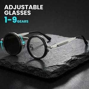 Op de afbeelding: Verstelbare bril met ronde glazen en zilverkleurige metalen monturen. De tekst ADJUSTABLE GLASSES 1-9 GEARS is zichtbaar. De bril heeft een mechanisch tandwielsysteem op de pootjes en zwarte randen rond de ronde glazen.