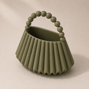 May include: An olive green handbag with a pleated, fan-like body and a top handle constructed from a series of smooth, spherical beads. The bag features a wide, open top and a structured, accordion-style design with vertical folds throughout the exterior.