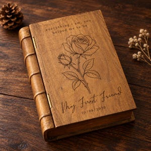 May include: A rectangular wooden box designed to resemble a book, featuring a laser-engraved rose illustration. The text reads: everything i am, you helped me to be, My First Friend, and the date 10/08/2030. The wood has a natural grain.